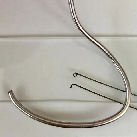 Metal plating and colony-picking tools on a white surface: a bent spreader and two fine wire picks, one with a loop